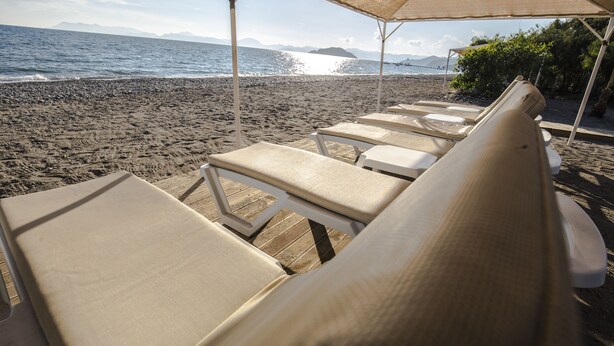 Eine Strandlounge mit Liegestühlen unter einem Sonnensegel, mit Blick auf das Meer.