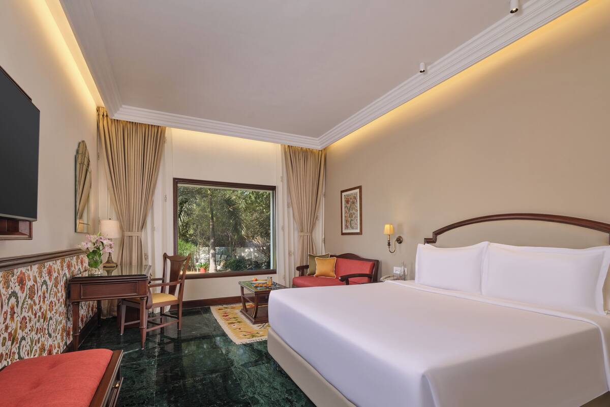 A hotel room with a large bed, a desk, a chair, a small table, and a window with curtains.