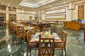 A spacious hotel dining area with multiple tables and chairs, a central bar, and decorative wall art. - The Ummed Ahmedabad Airport (Ahmedabad)