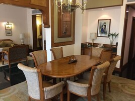 Un comedor con una mesa de madera y seis sillas tapizadas. Encima de la mesa, un candelabro; en la pared, un cuadro enmarcado; y sobre una mesita auxiliar, una planta.