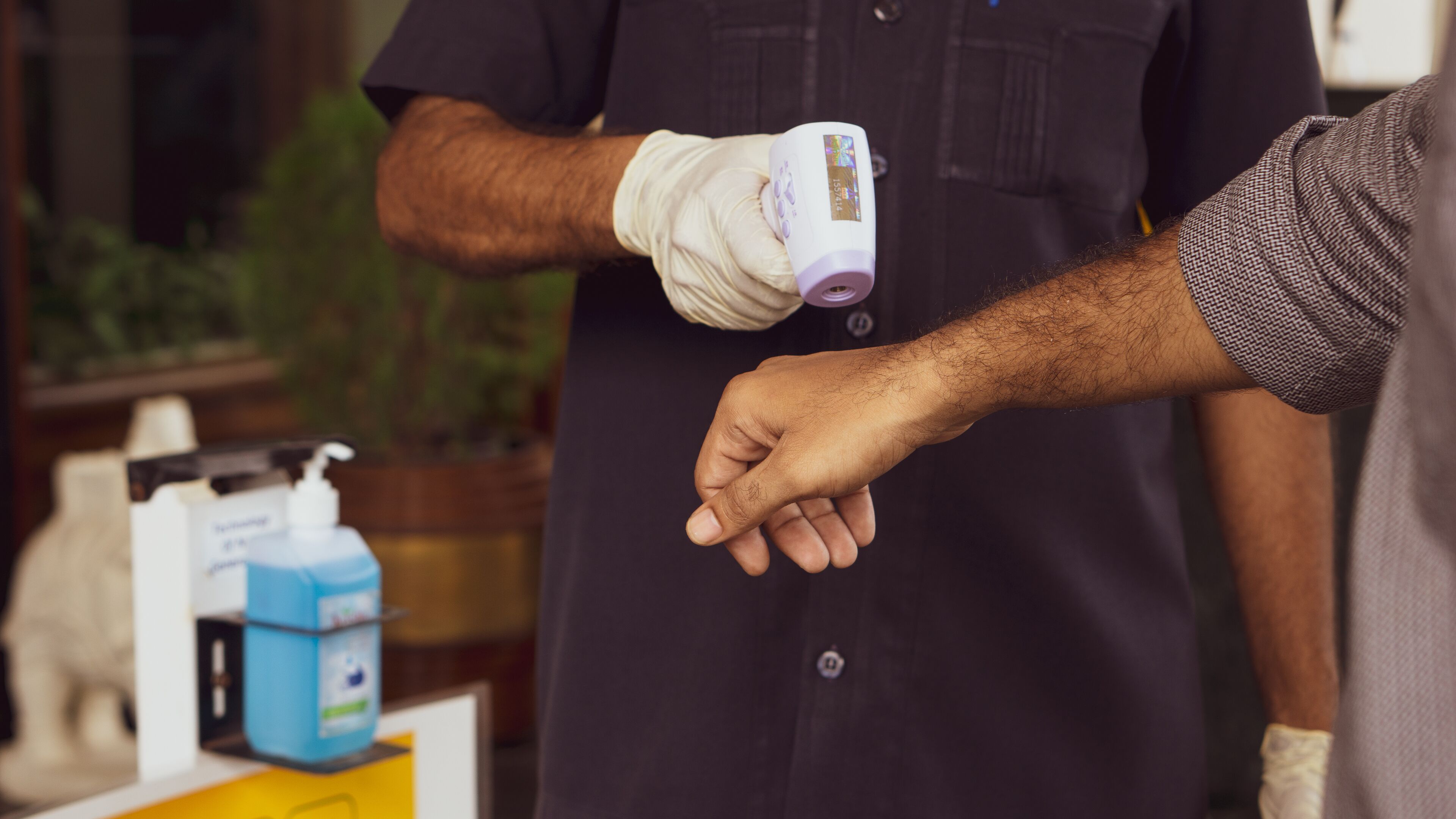 A person wearing a dark shirt and white gloves, holding a device near another person's hand.
