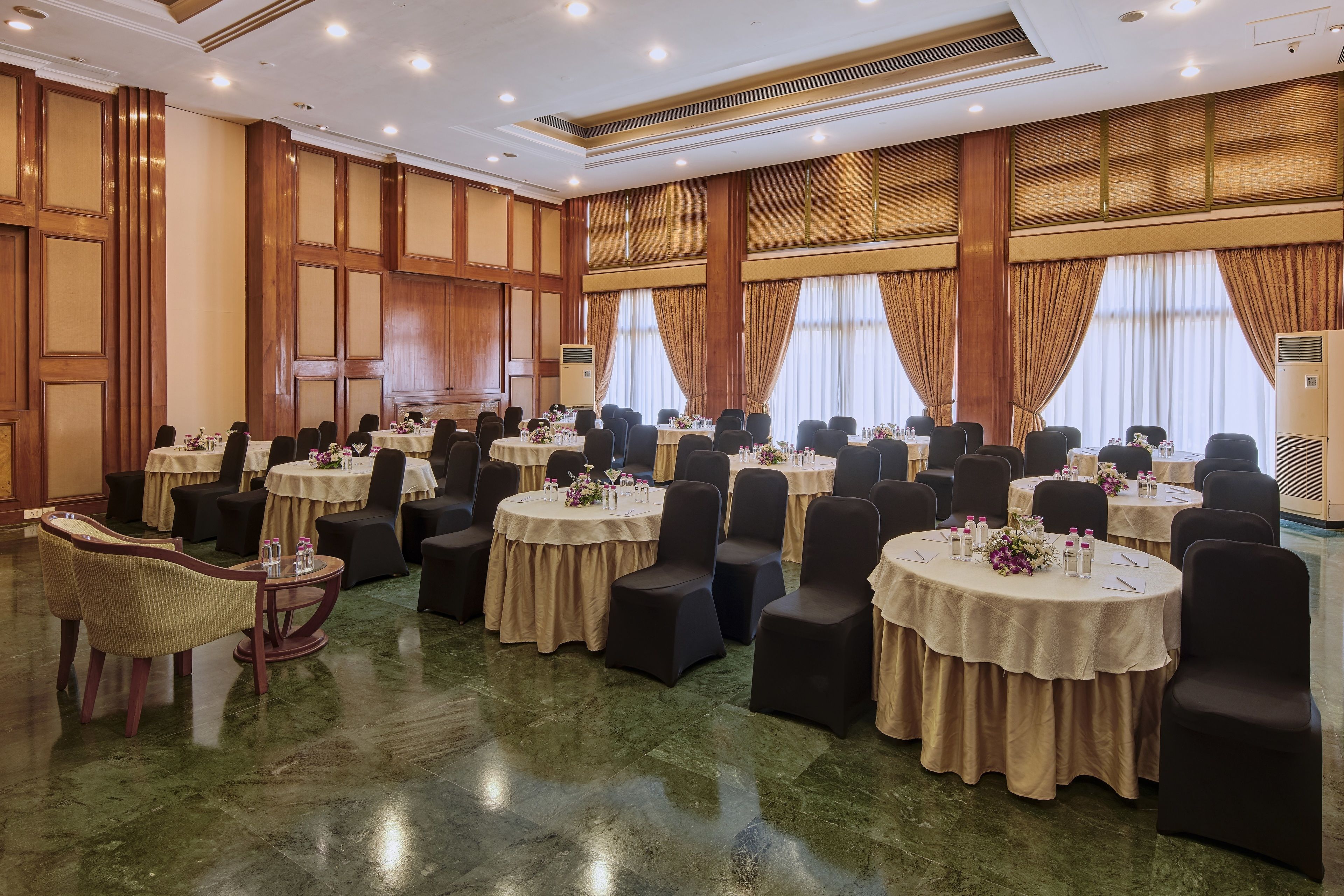 A banquet hall with multiple round tables, black chairs, and beige tablecloths.
