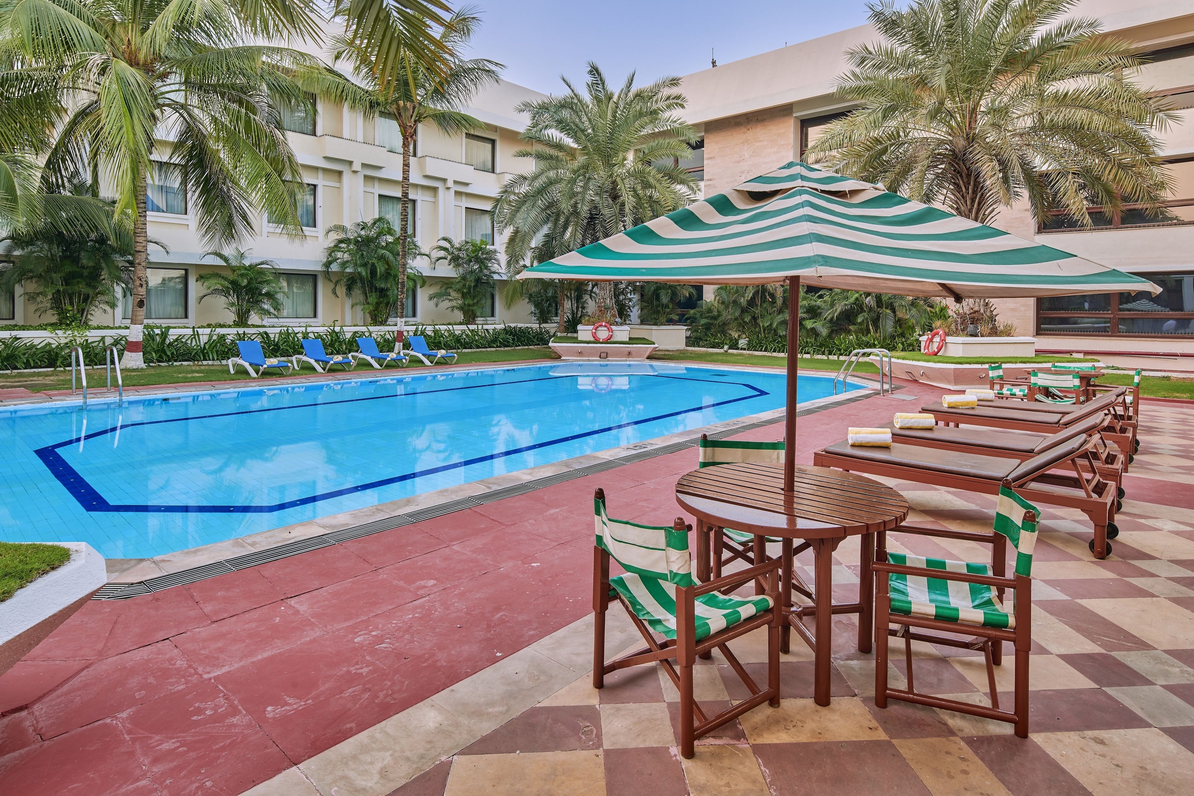 Un área de piscina con sillones de descanso y mesas, piscina e incluso palmeras.