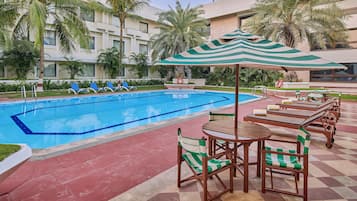 Un área de piscina con sillones de descanso y mesas, piscina e incluso palmeras.