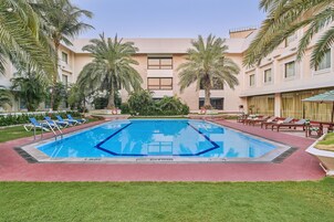 A swimming pool surrounded by palm trees and lounge chairs, with a building in the background.