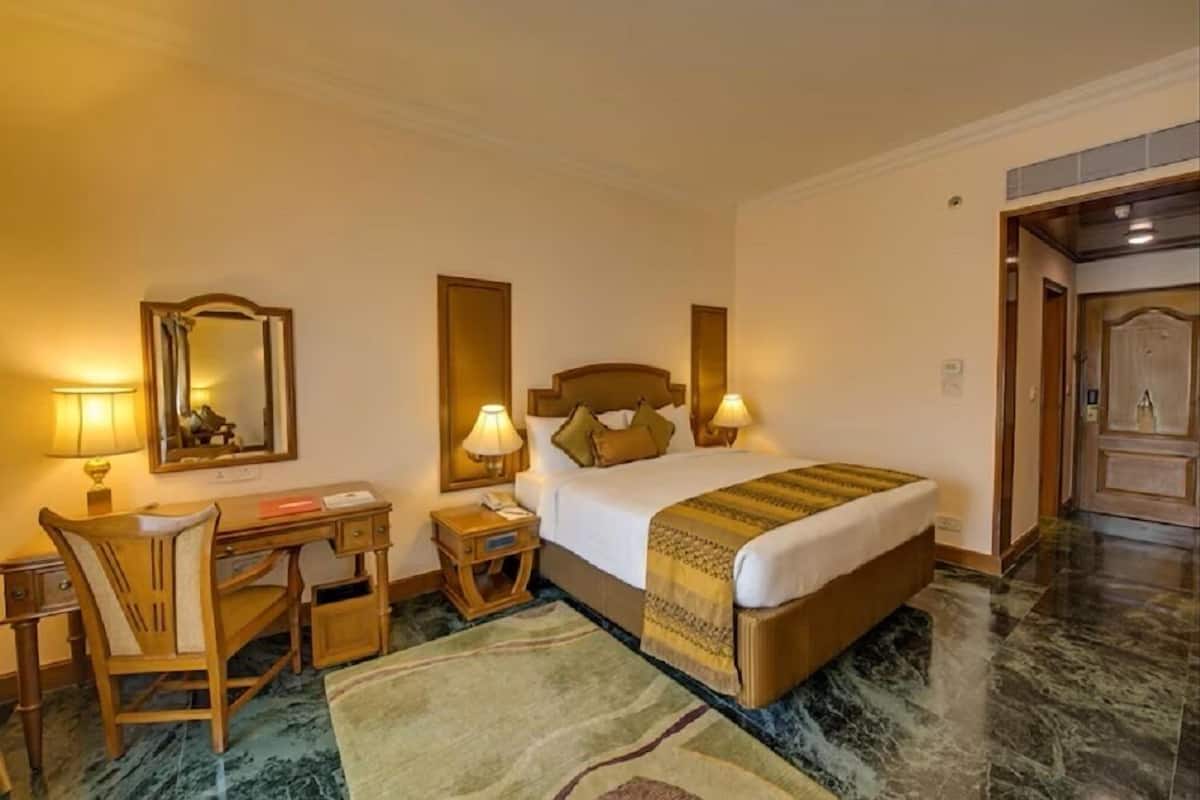 A hotel room with a bed, desk, chair, bedside lamps, and a mirror.