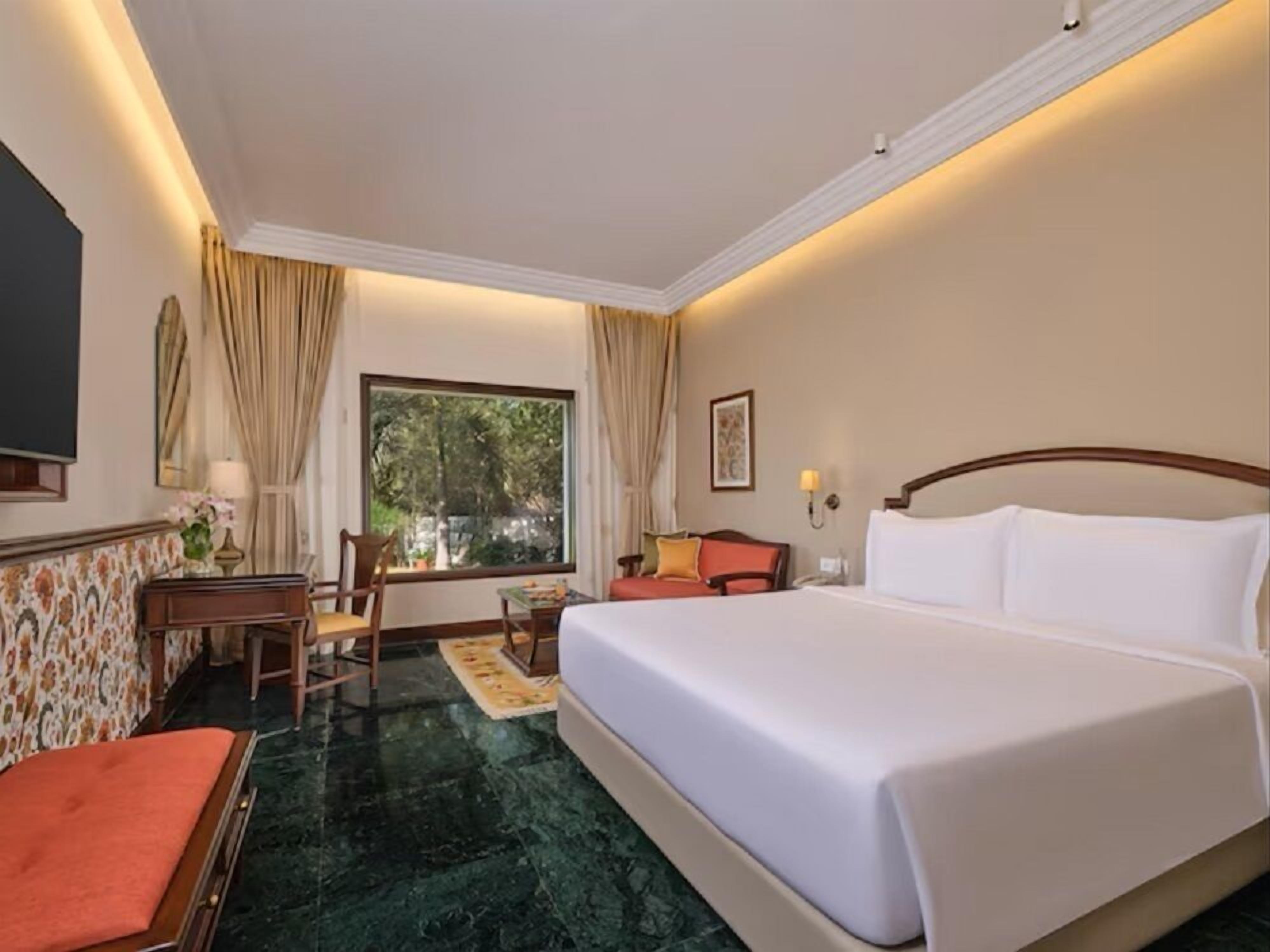 Une chambre d’hôtel avec un lit, un bureau, une chaise, une fenêtre avec des rideaux et une vue sur la verdure.