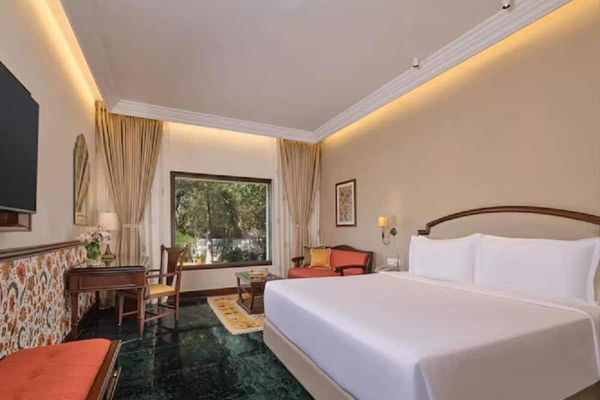 Une chambre d’hôtel avec un lit, un bureau, une chaise, une fenêtre avec des rideaux et une vue sur la verdure.