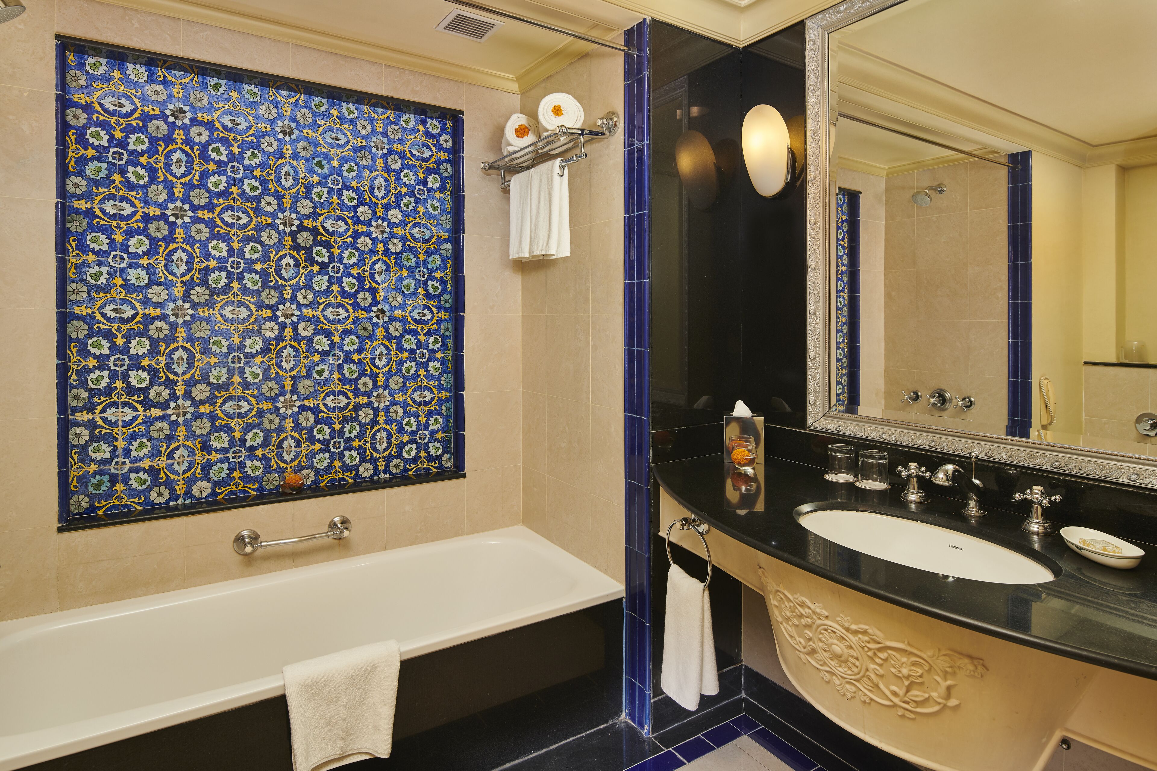 A bathroom with a large mirror, a bathtub, a sink, and a decorative tile wall.