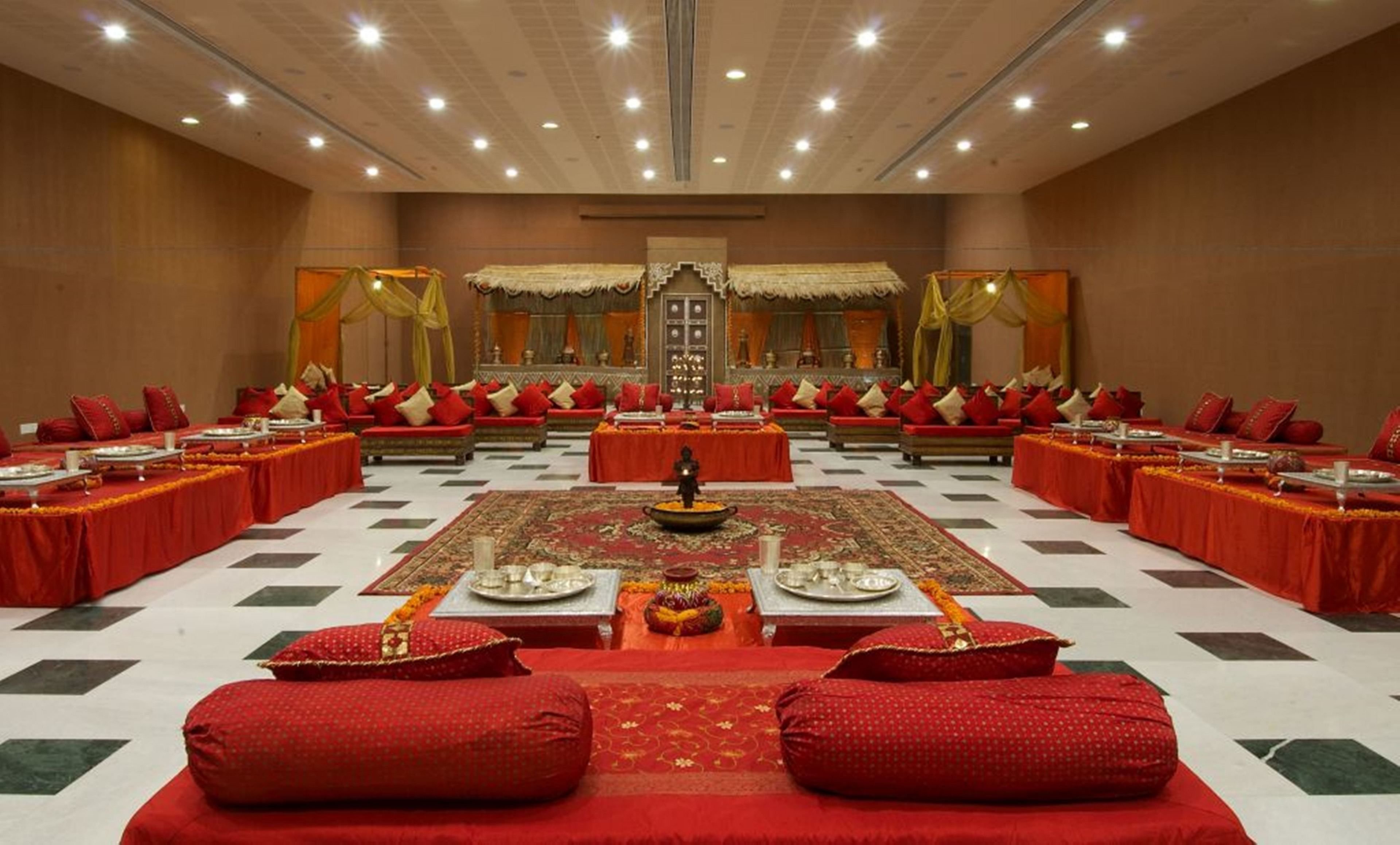 A large conference room with a central table, surrounded by rows of red sofas and tables, and a patterned carpet.