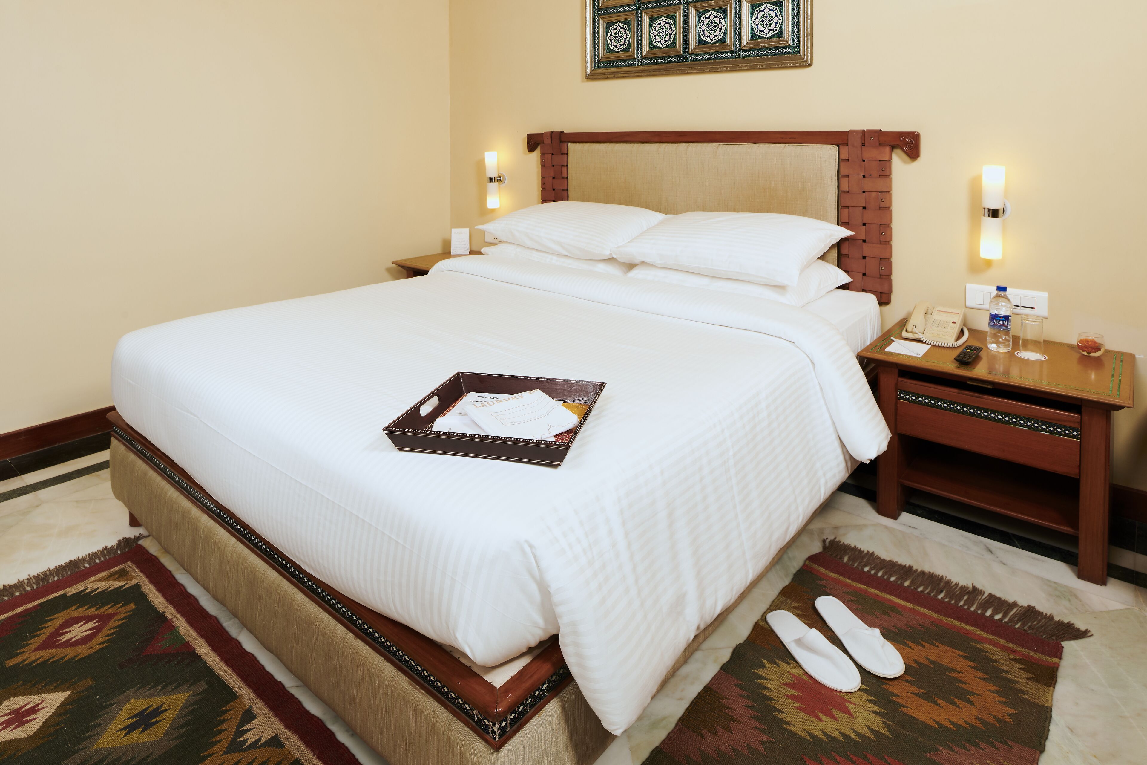 A neatly made bed with a tray of toiletries, a bedside table with a lamp, and a wall-mounted phone.