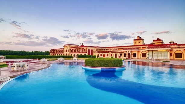 A large swimming pool with a central island, surrounded by a building with multiple balconies and a red roof. - The Ummed Jodhpur Palace Resort & Spa (Jodhpur)