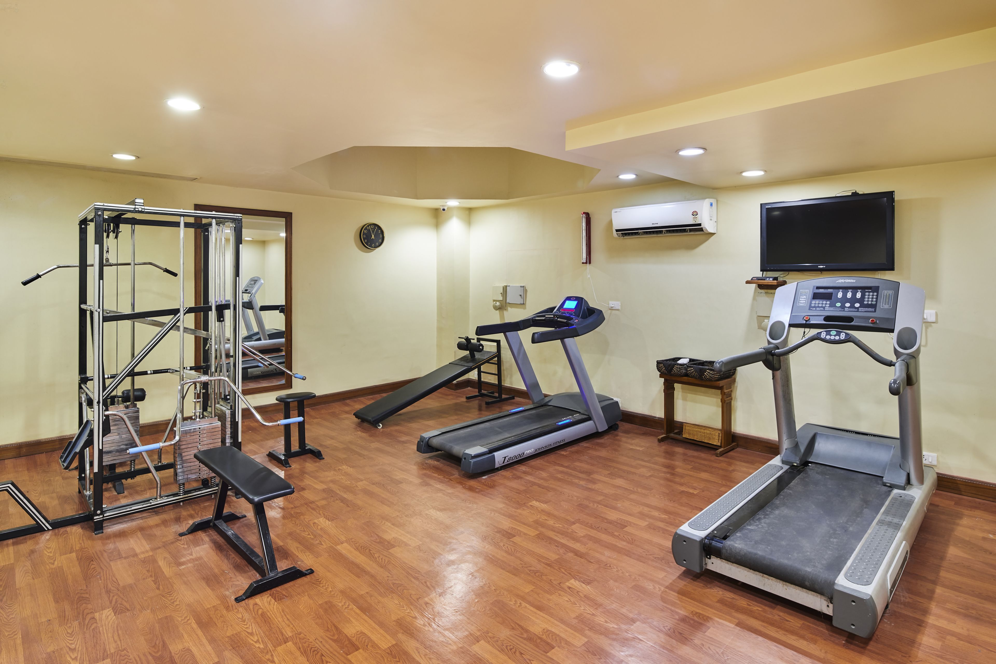 A home gym with a treadmill, bench press, and weight machine.