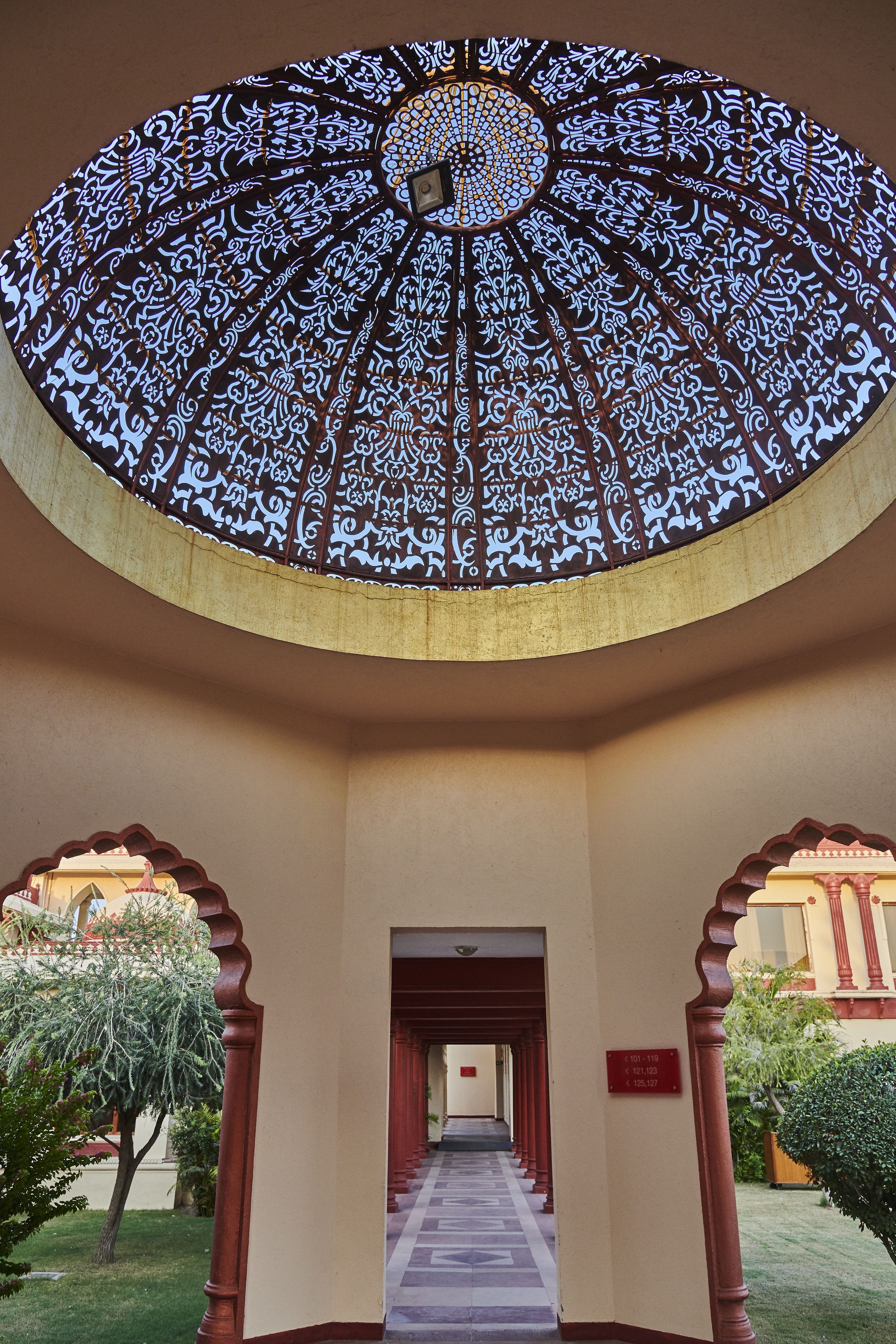 Un corridoio con soffitto decorato e archi, che conduce a una porta con un cartello.