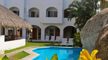 A resort with a swimming pool, white buildings, and a thatched-roof structure.
