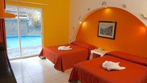 A hotel room with two beds, a small table, a telephone, and a window with a view of a pool.