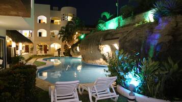 Una piscina con sillas de descanso, una pared de roca y un edificio con varios balcones.