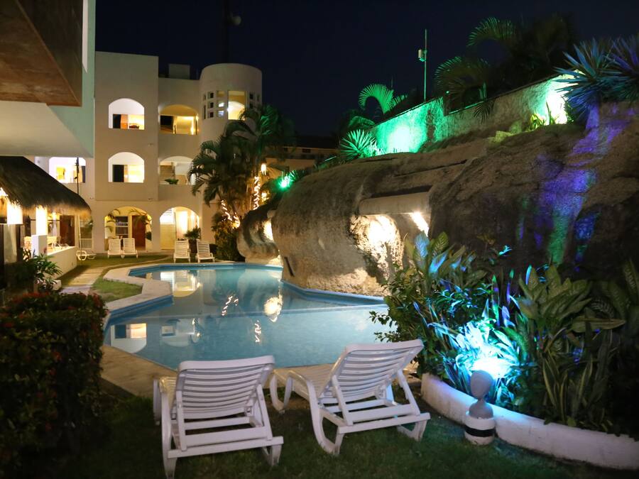 Una piscina con sillas de descanso, una pared de roca y un edificio con varios balcones.