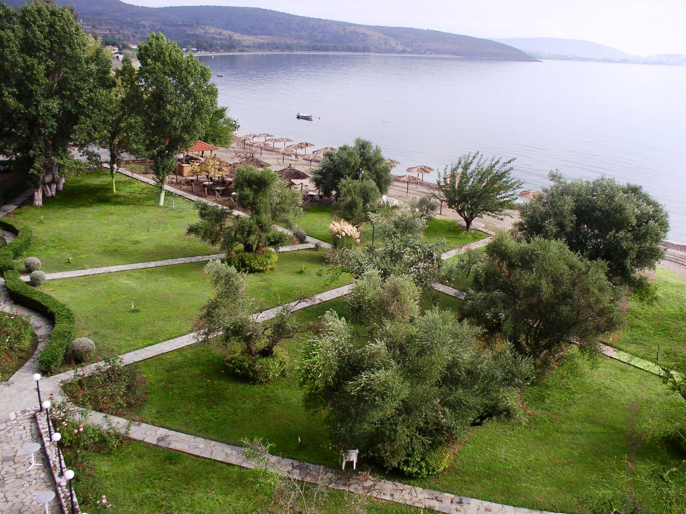 Un giardino curato con vialetti, alberi e vista su un lago con barche.