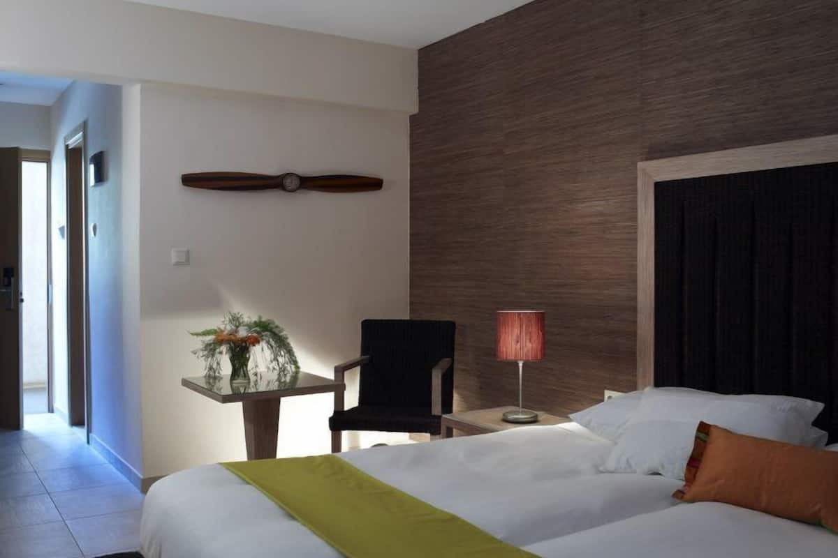 Camera d'albergo con un letto, una poltrona, un tavolino con un vaso di fiori, una lampada e un pannello di legno al muro.