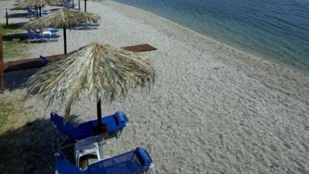 A beach with clear blue water, a sandy shore, and several blue lounge chairs under thatched umbrellas. - Belle Helene Hotel (East Mani)