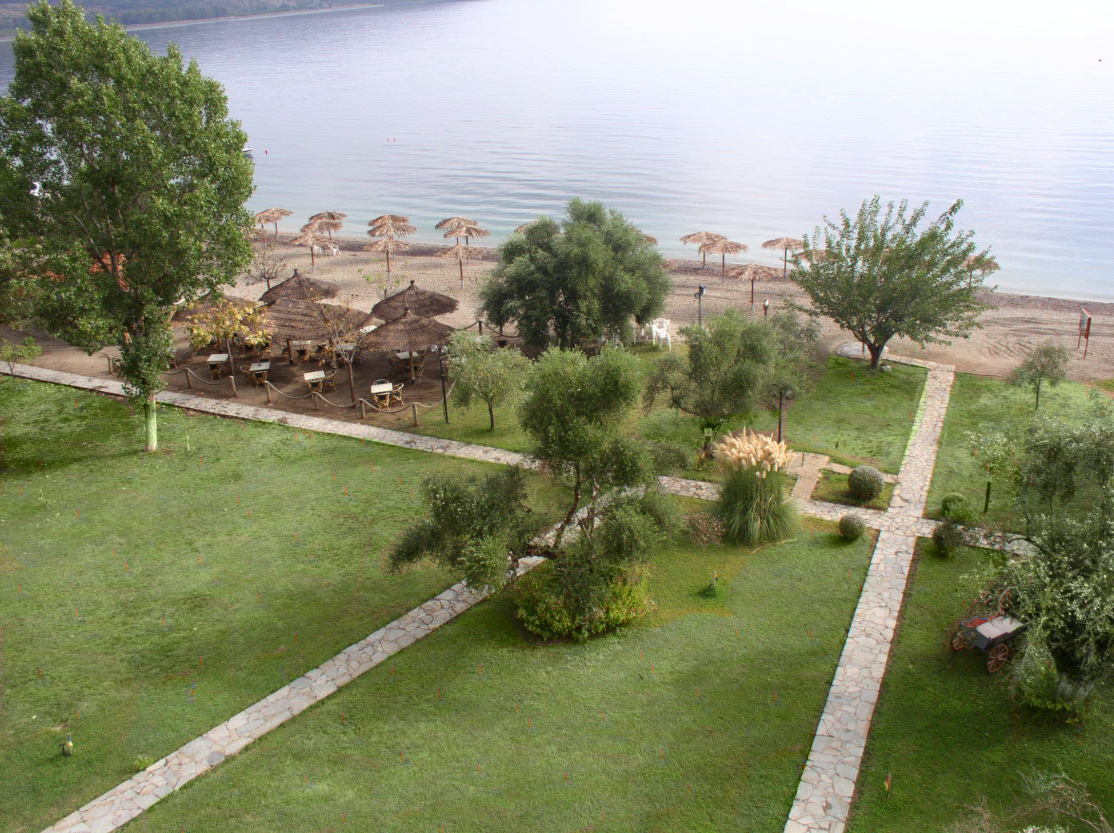 A landscaped area with a stone pathway, grassy areas, and a row of thatched umbrellas along a lakeside.