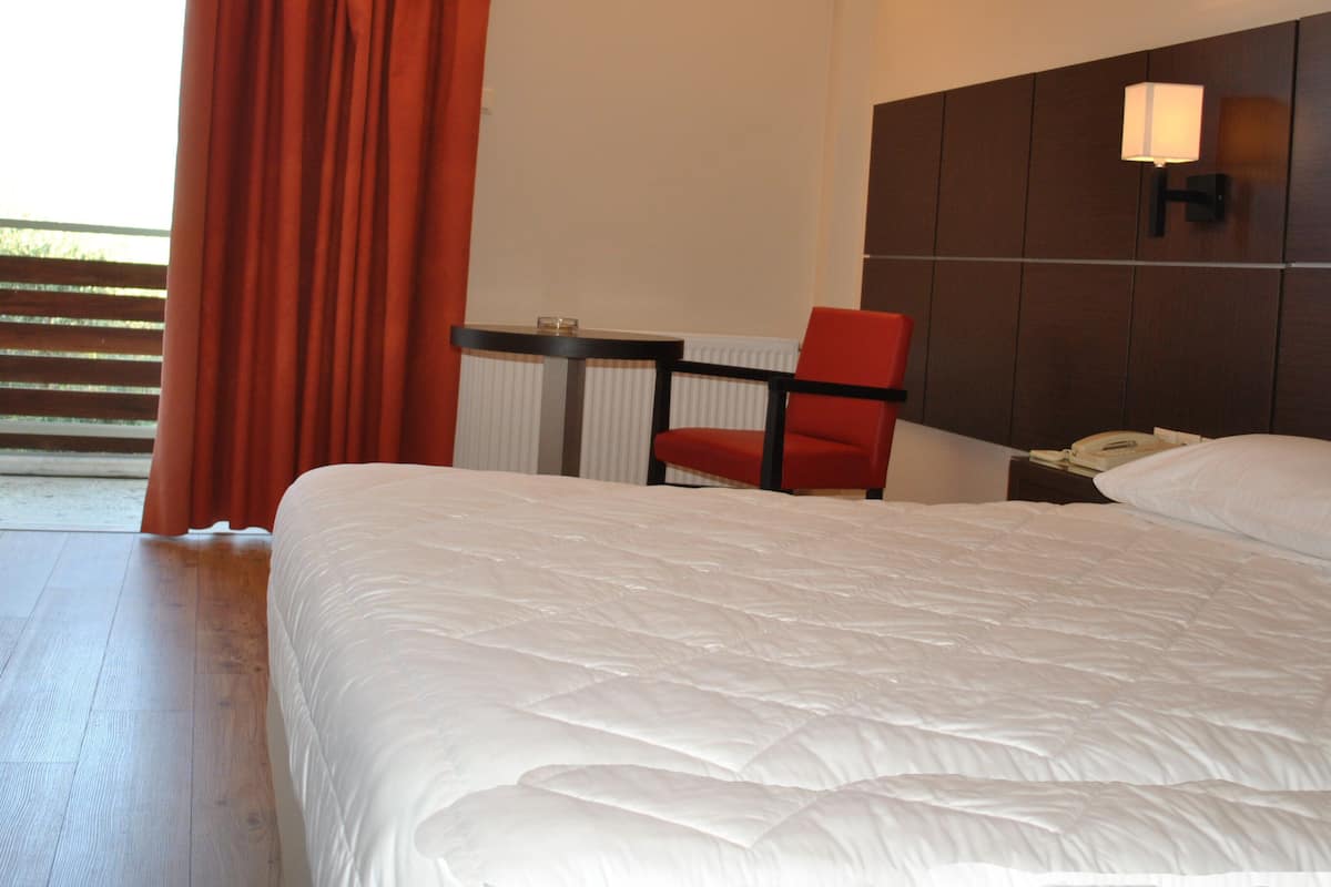 Una camera d'albergo con un letto grande, una scrivania con una sedia, un telefono sul comodino e una finestra con tende.