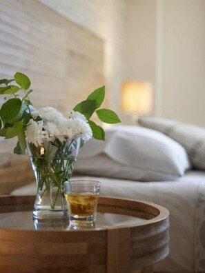 A clear glass vase with white flowers and green leaves on a wooden table. - Belle Helene Hotel (East Mani)