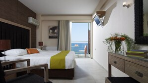A hotel room with a bed, a desk, a chair, a TV, a plant, and a view of the sea. - Belle Helene Hotel (East Mani)
