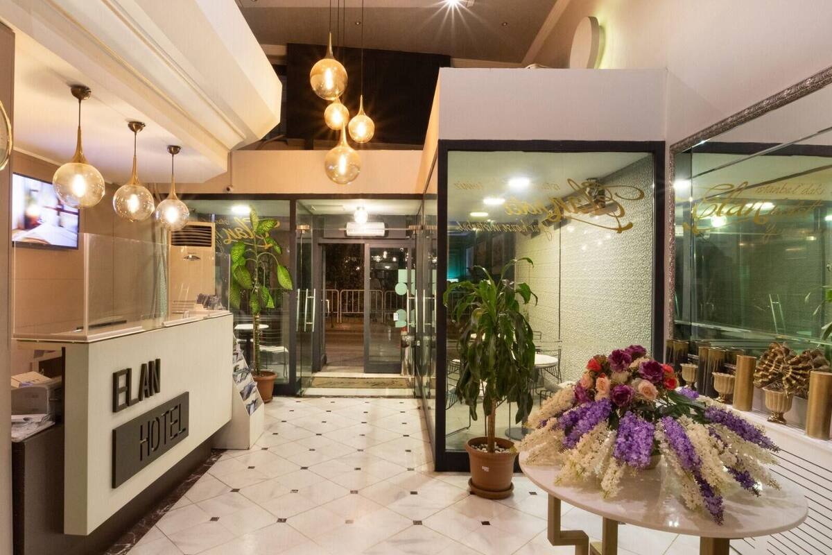 A hotel reception area with a reception desk, a large potted plant, and a table with a floral arrangement.