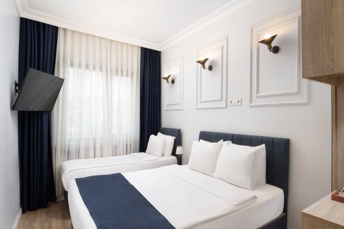 A hotel room with two beds, a flat-screen TV, and a large window with curtains.