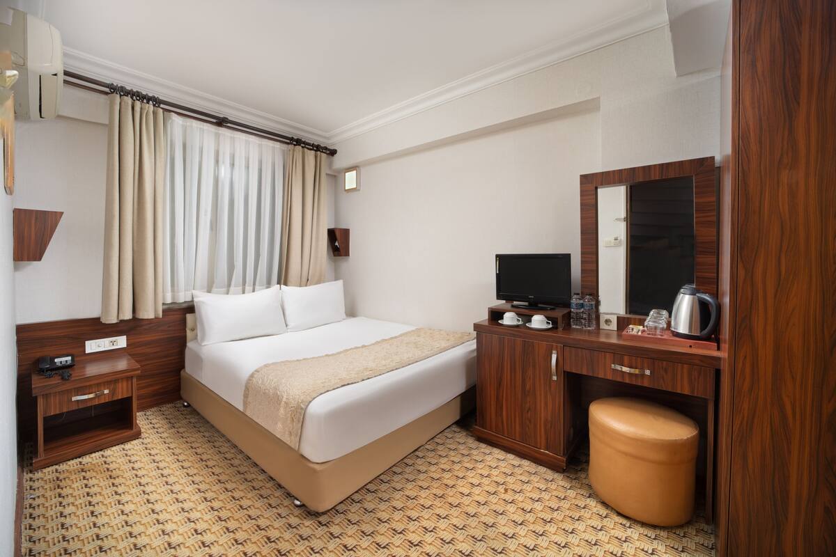 A hotel room with a bed, wooden nightstand, TV, and a small wooden cabinet with a mirror.