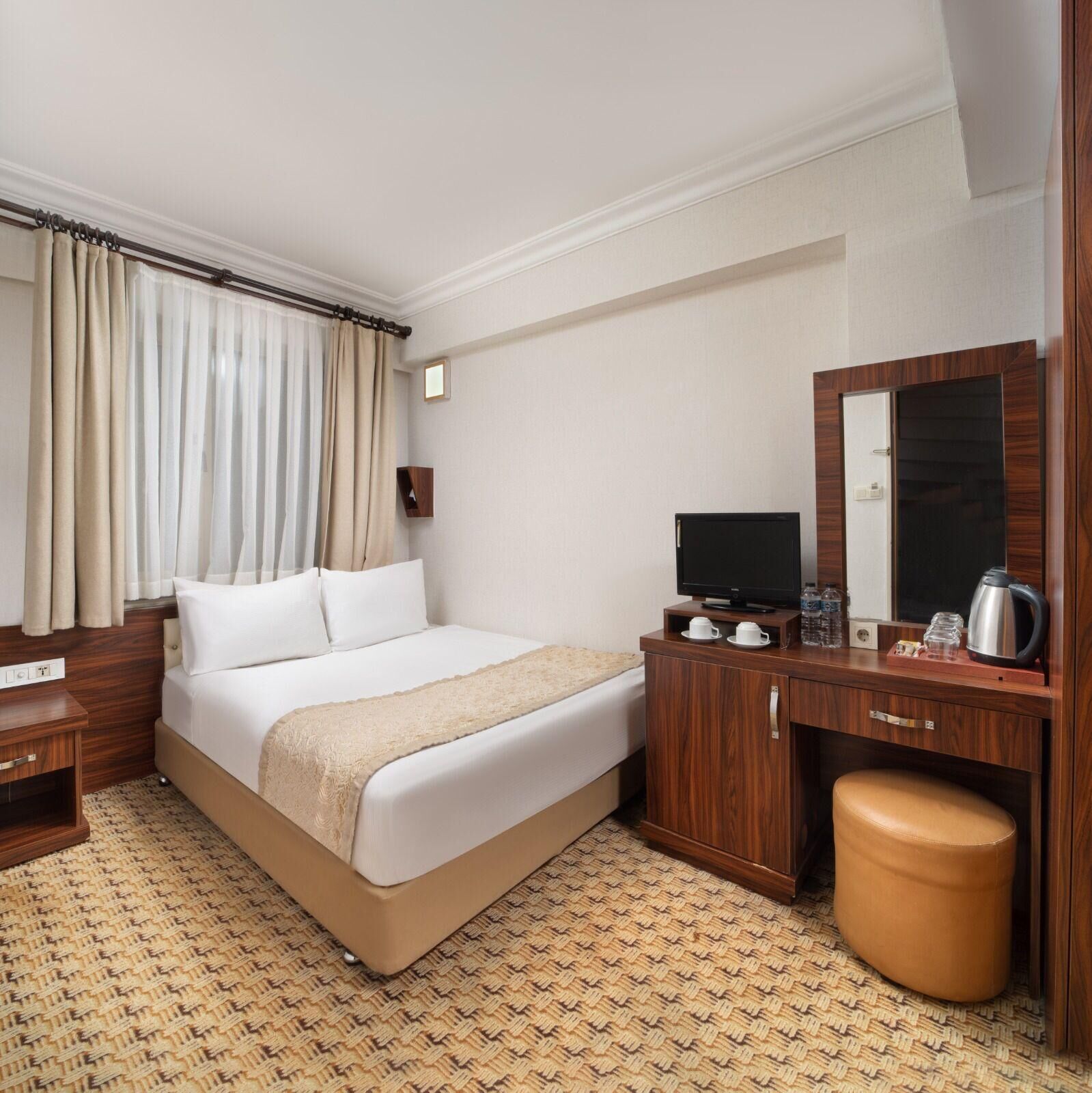 Ein Hotelzimmer mit einem Bett, einem Fernseher, einem Schreibtisch, einem Spiegel und einem kleinen Hocker.