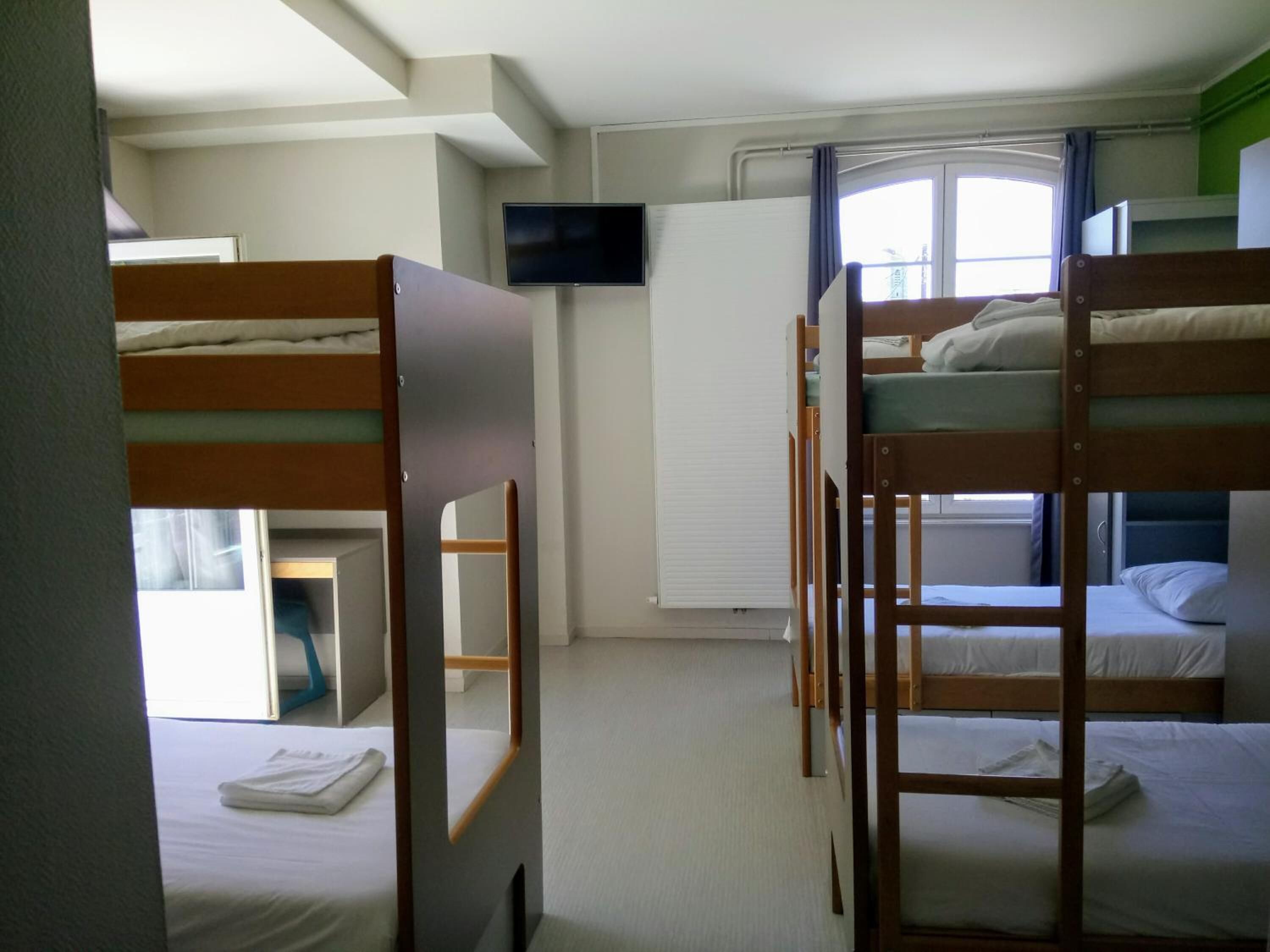 A dormitory room with bunk beds, a television, and a window with curtains.