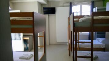 A dormitory room with bunk beds, a television, and a window with curtains.