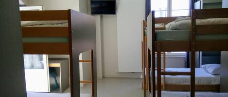 A dormitory room with bunk beds, a television, and a window with curtains.