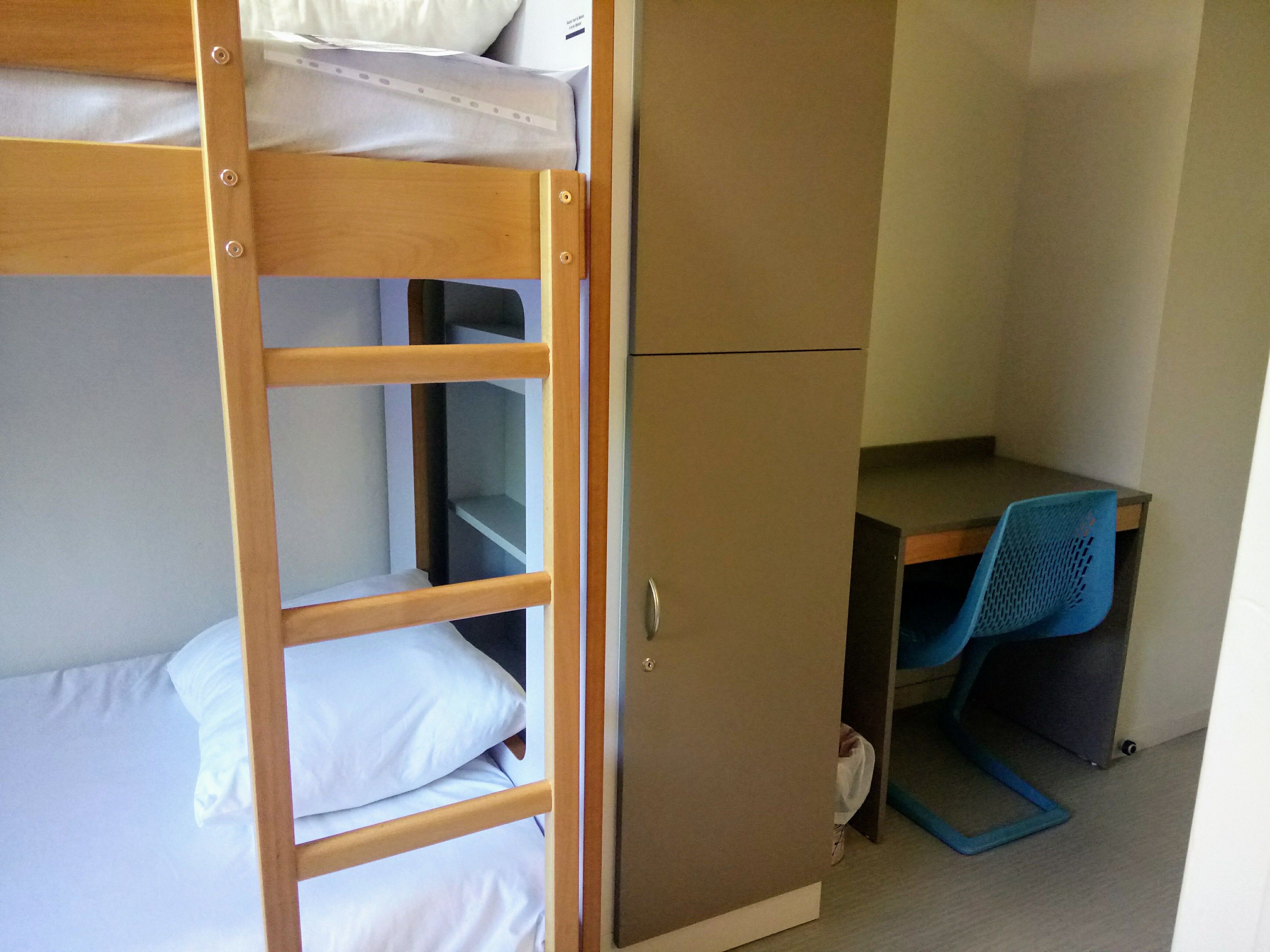 A bunk bed with a ladder, a desk with a chair, and a wardrobe.