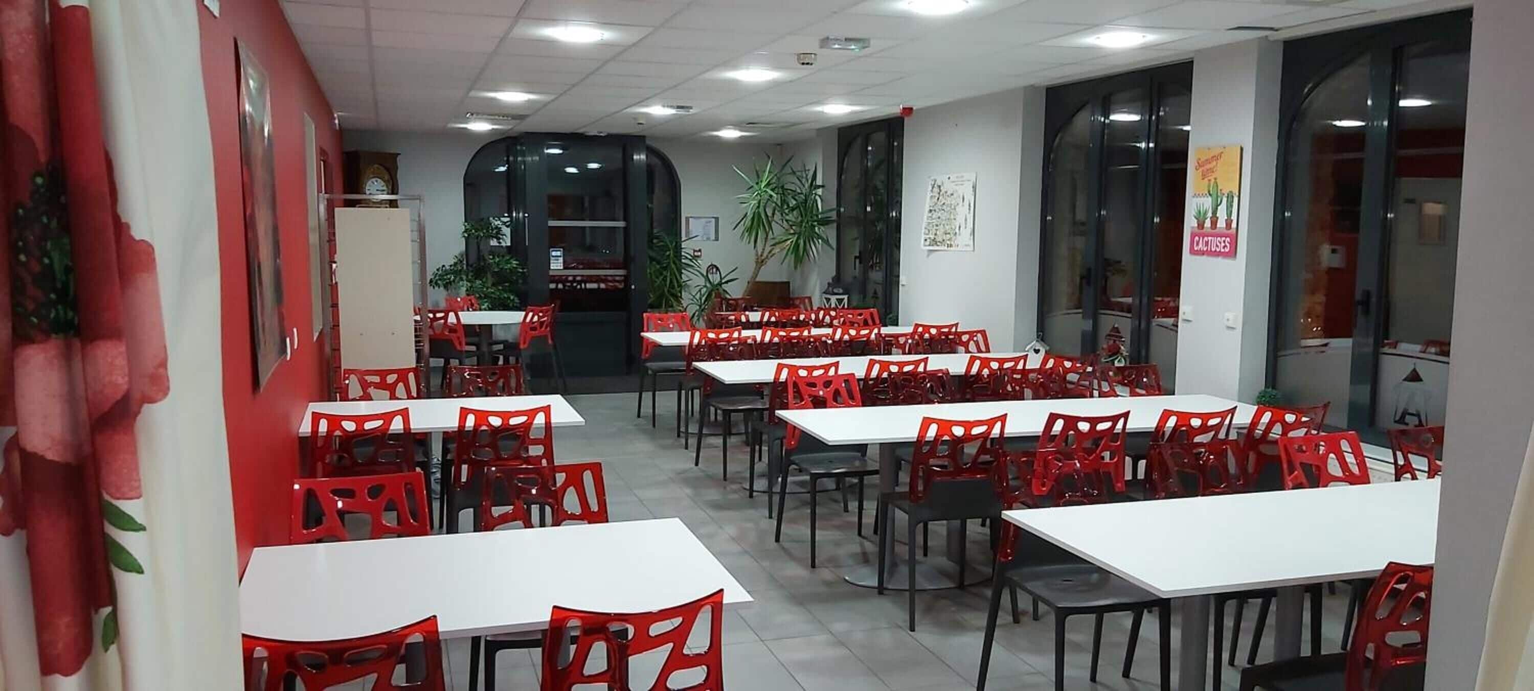 Un comedor con mesas y sillas, una planta en maceta y un cartel en la pared.