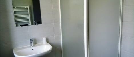 Un baño con lavamanos pedestal blanco, espejo y cabina de ducha.