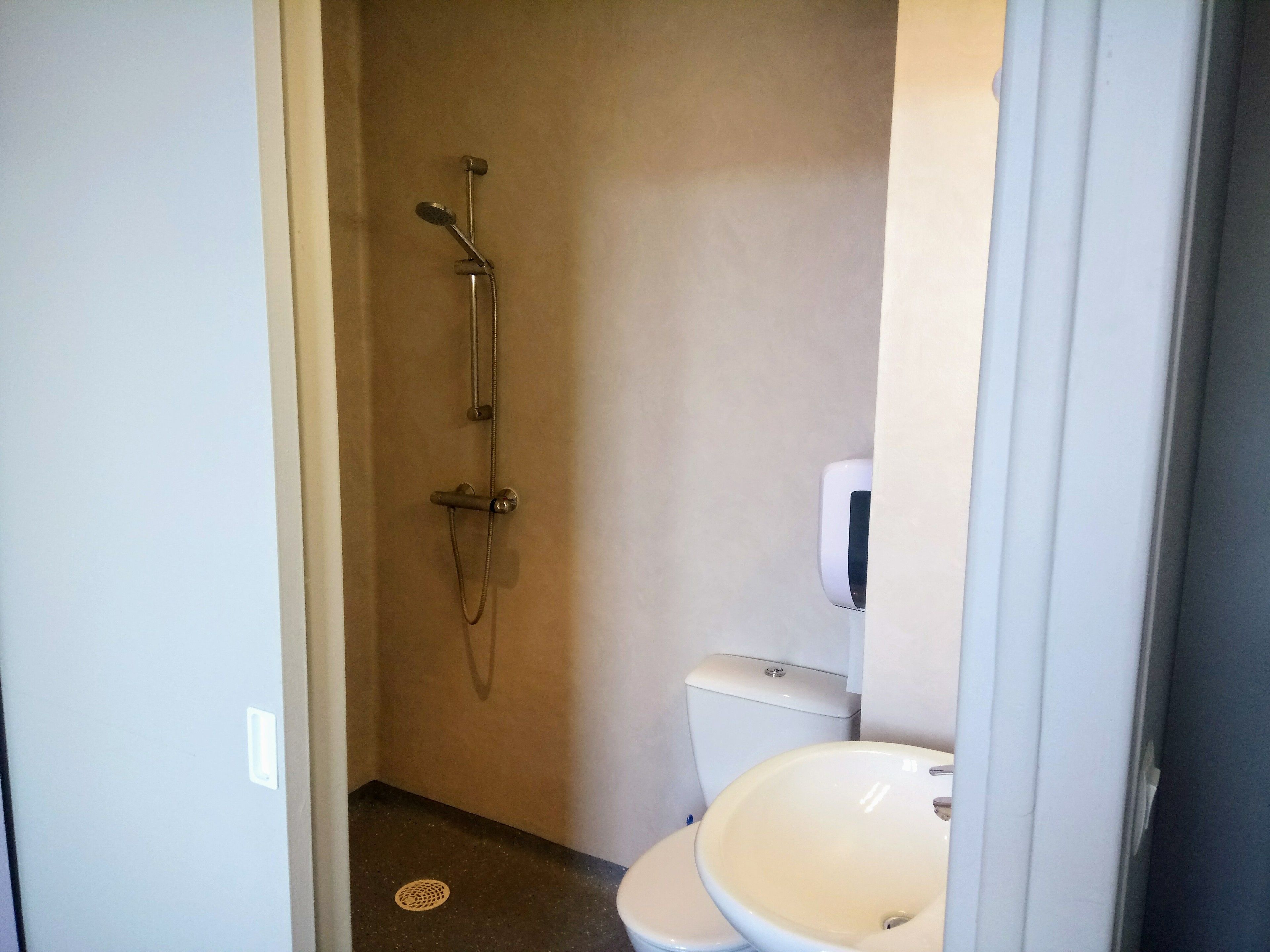 Et lille badeværelse med brusebad, toilet og vask.