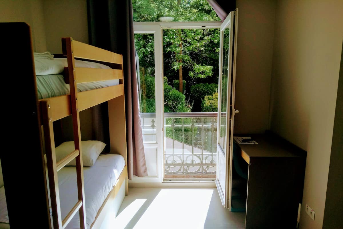 Ein Zimmer mit einem Etagenbett, einem Schreibtisch und einem Balkon mit Blick ins Grüne.