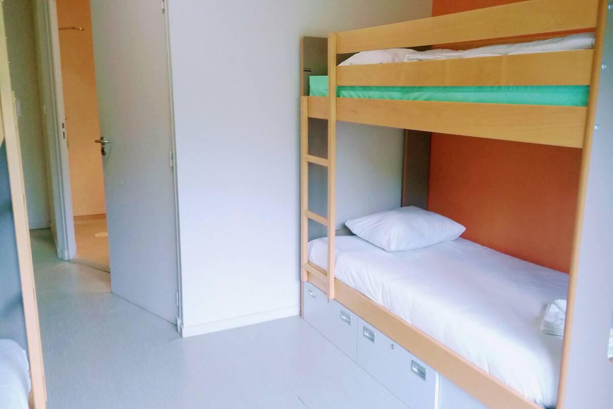 Ein Etagenbett mit unterem Stockbett und einem Einzelbett, eine Holzleiter und eine kleine Ablage.