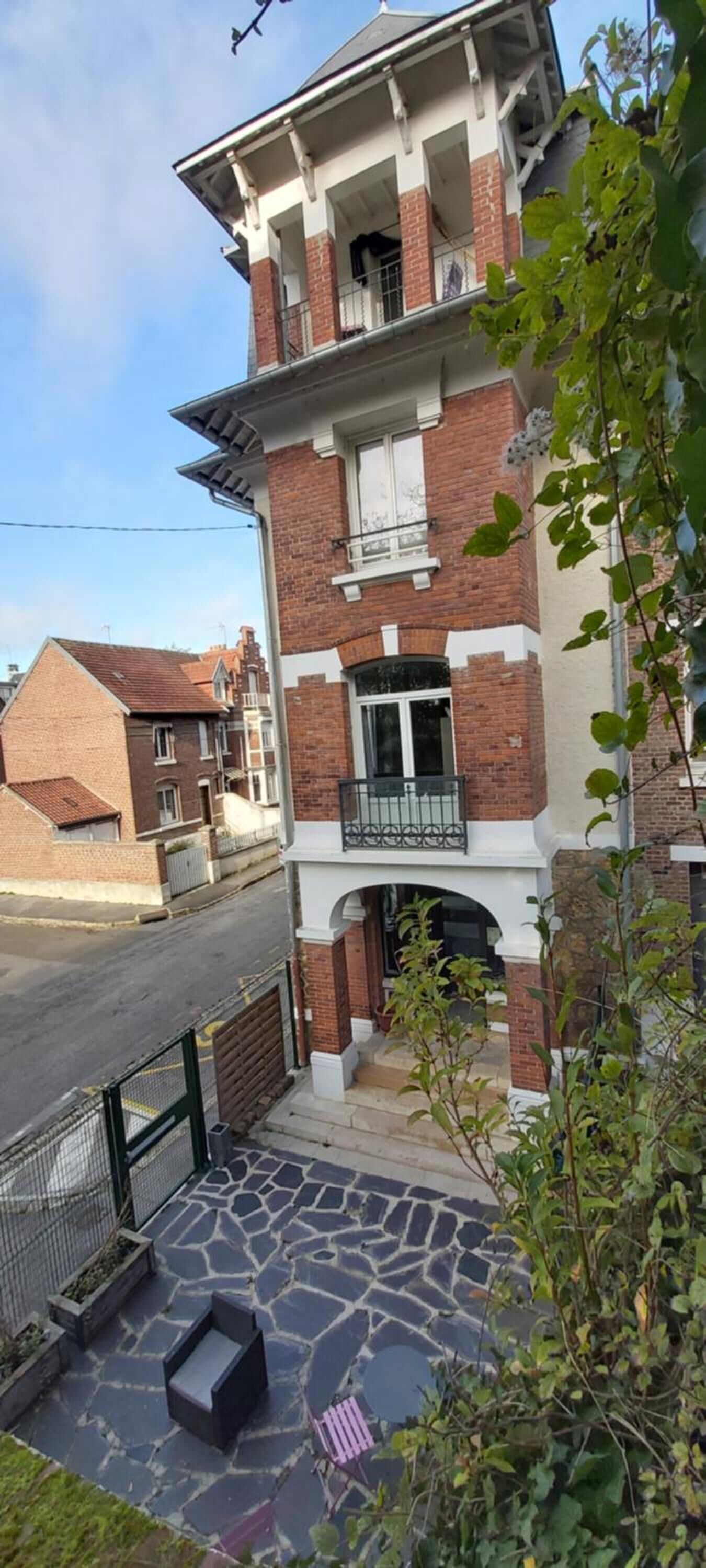 A two-story residential building with a balcony, a stone-paved entrance, and a metal gate.