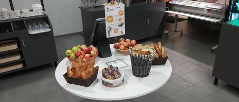 A buffet setup with various food items including fruits, pastries, and bread.