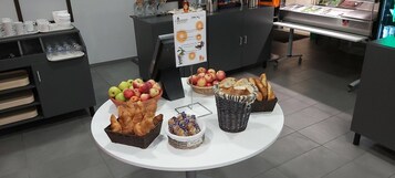 Montaje de bufé con diversos alimentos, entre ellos frutas, pasteles y pan.