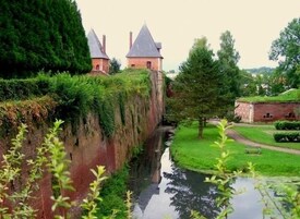 Un castillo con dos torres, un foso y un área arbolada y cubierta de césped.