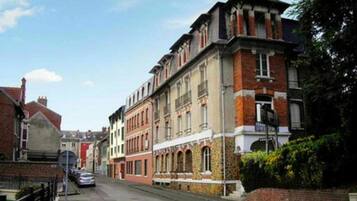 A street view of a row of historic buildings with a mix of architectural styles, including a prominent building with a corner turret and arched windows.