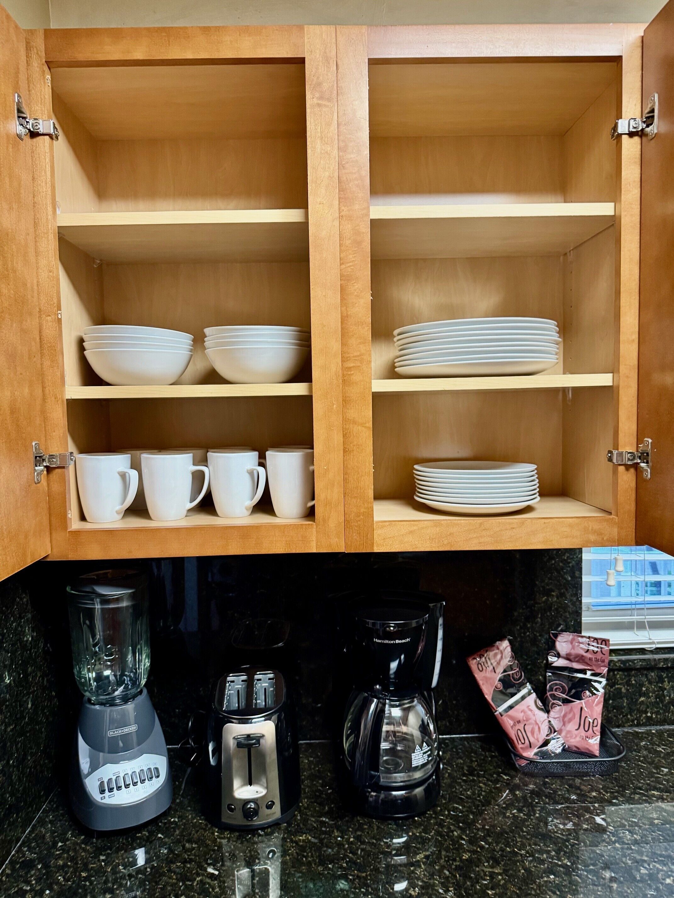 Een keuken met houten kastjes, witte kommen, witte bekers en een koffiezetapparaat.