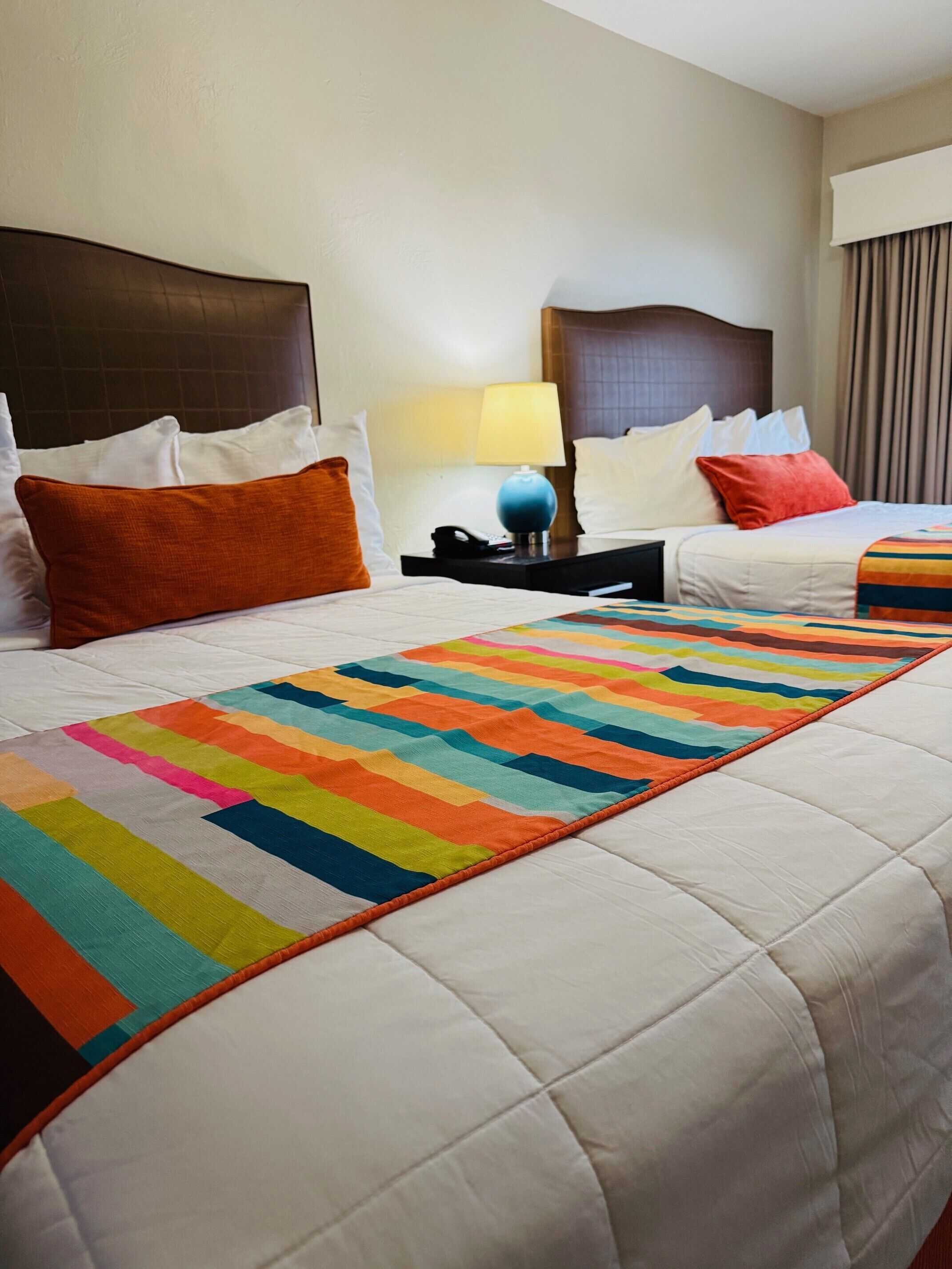 A hotel room with a large bed, a bedside table with a lamp, and a colorful quilt.