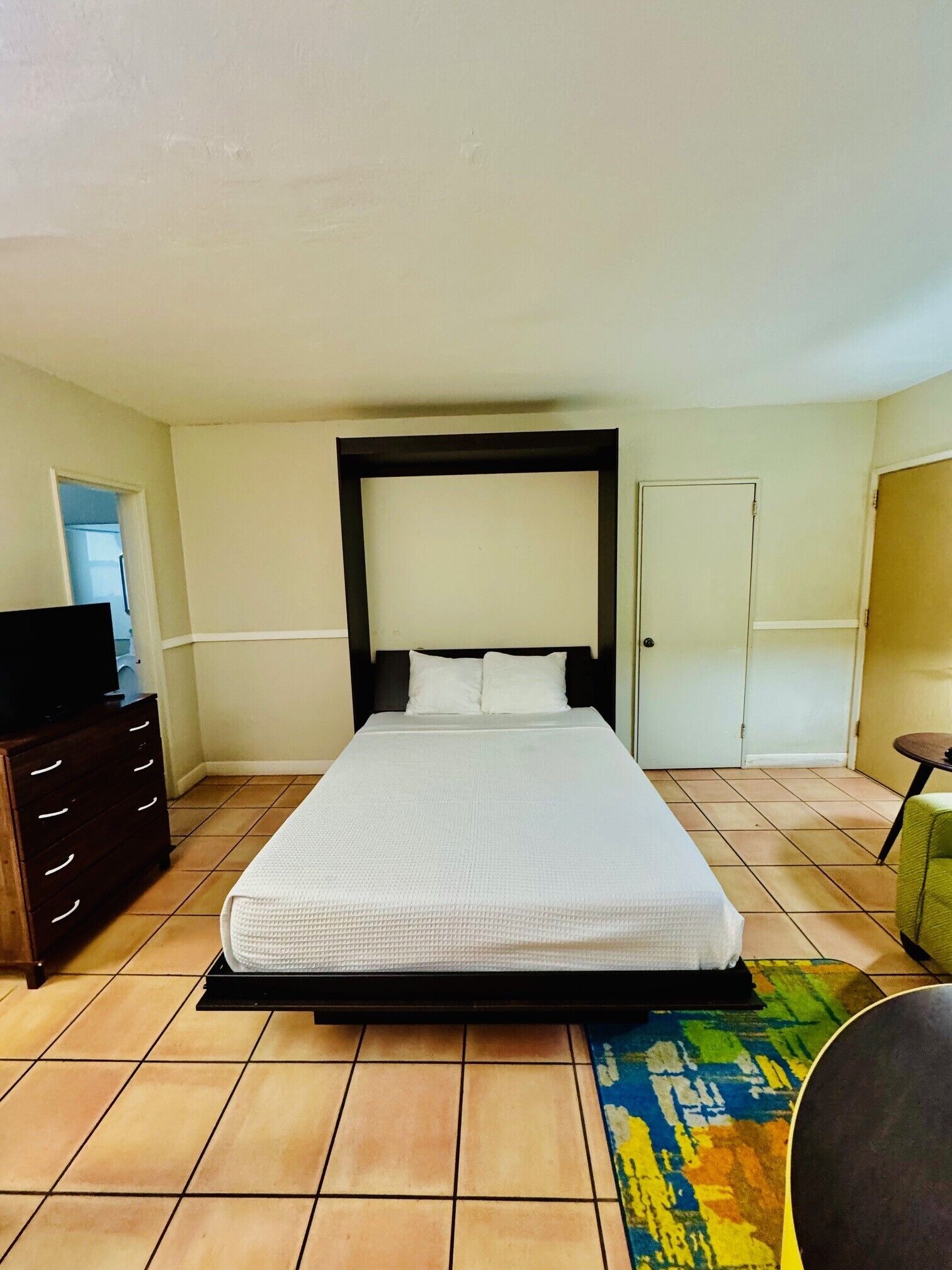 A bedroom with a bed, a dresser, a television, and a door.